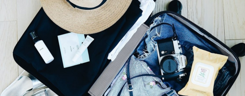 valise ouverte posée sur le sol avec vêtements, chapeau, lunette